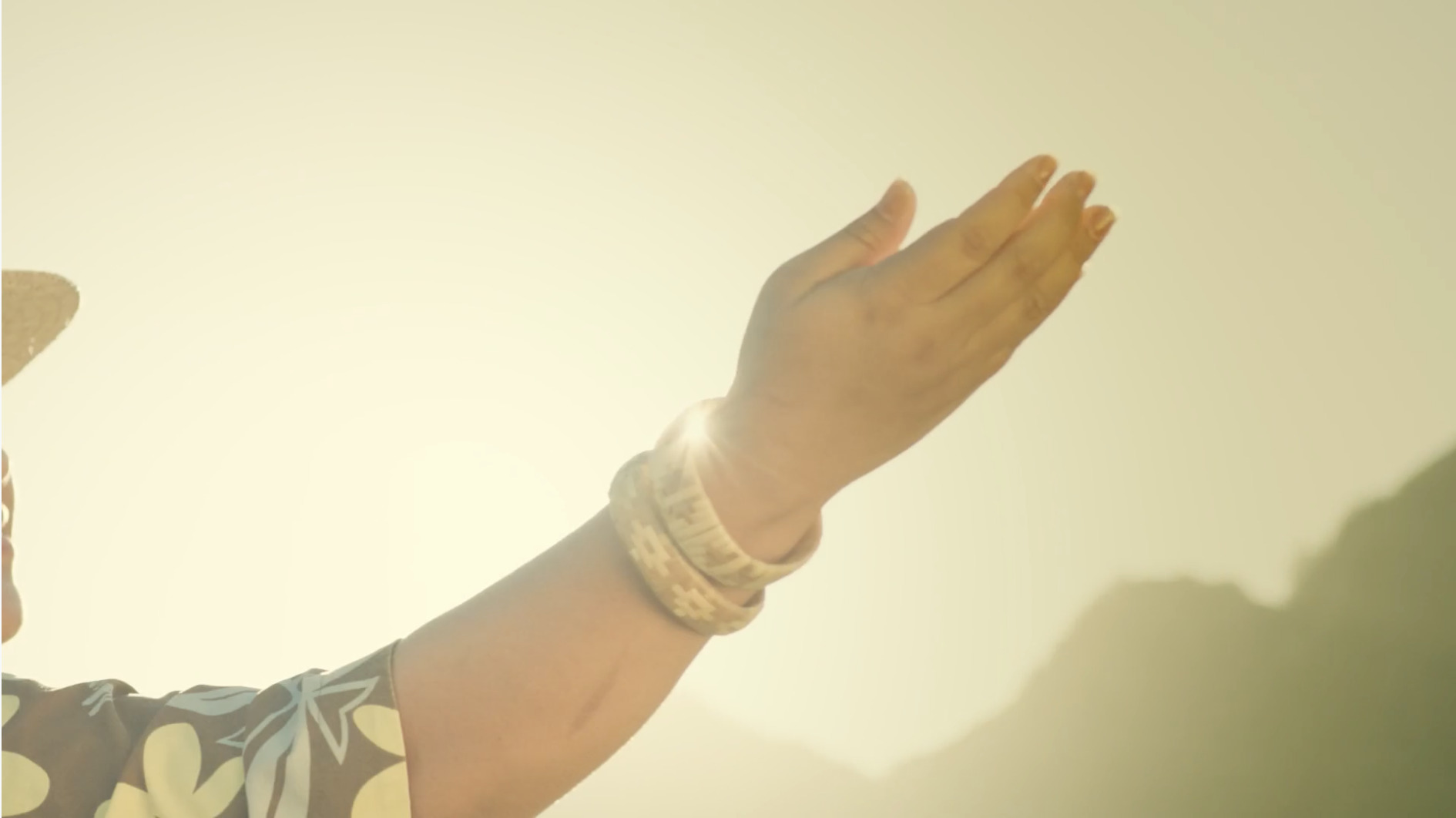 A dancer’s hand reaching into warm sunlight against the Koʻolau mountains